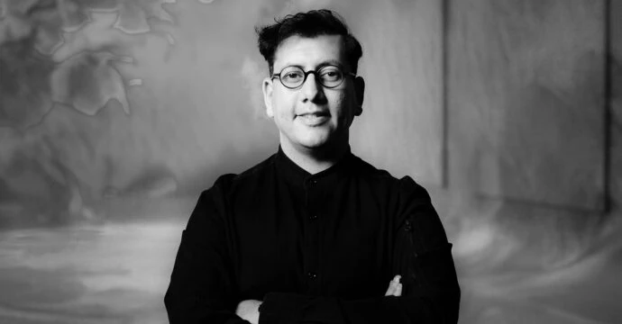 Black-and-white portrait of Refik Anadol wearing glasses, standing with arms crossed.
